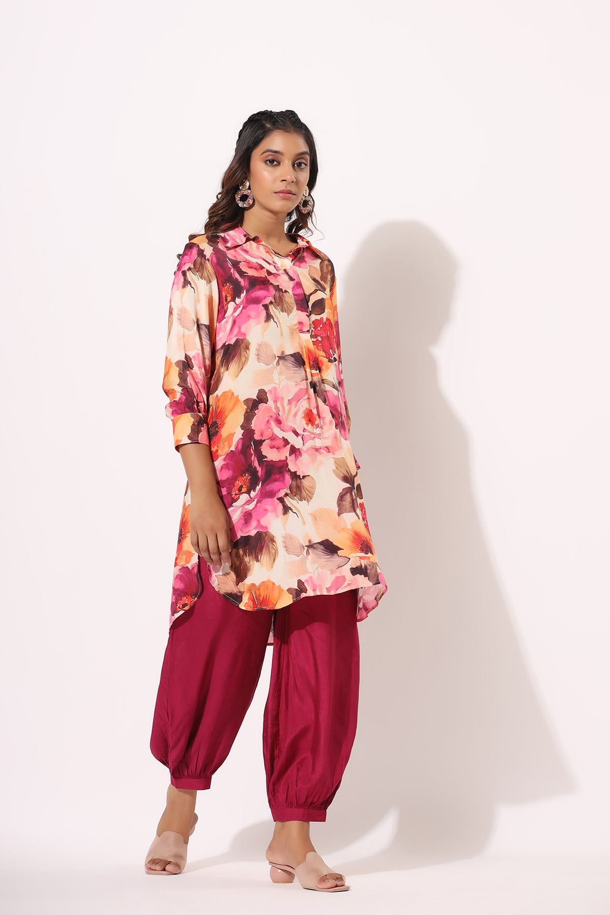 Woman wearing a colorful floral top and pink pants on a white background