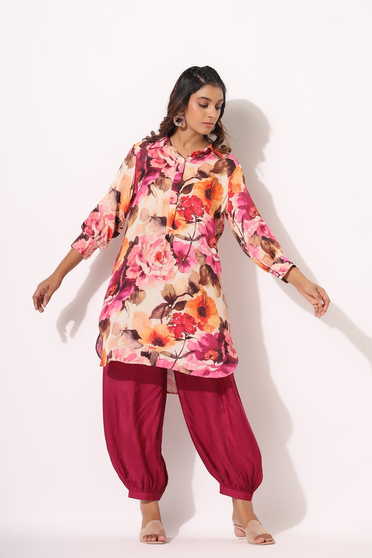 Woman wearing a floral pink and orange kurta with red pants on a white background
