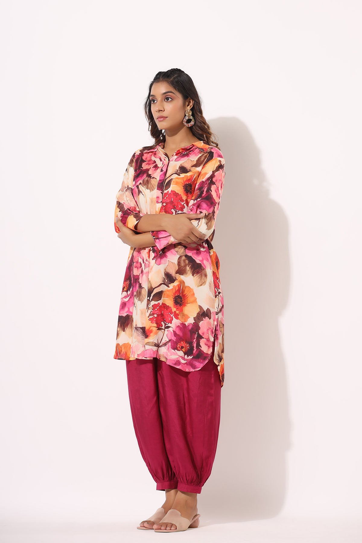 Woman wearing a colorful floral top and maroon pants on a white background