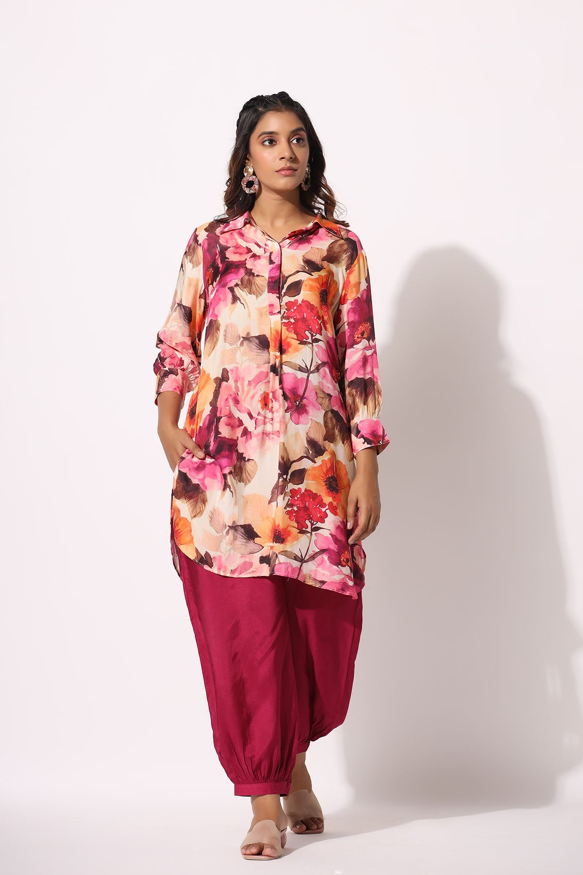 Woman wearing a colorful floral top and pink pants on a white background