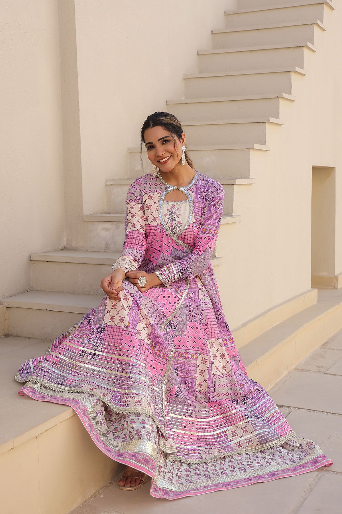 Woman in a pink and purple patterned dress sitting on steps outdoors.