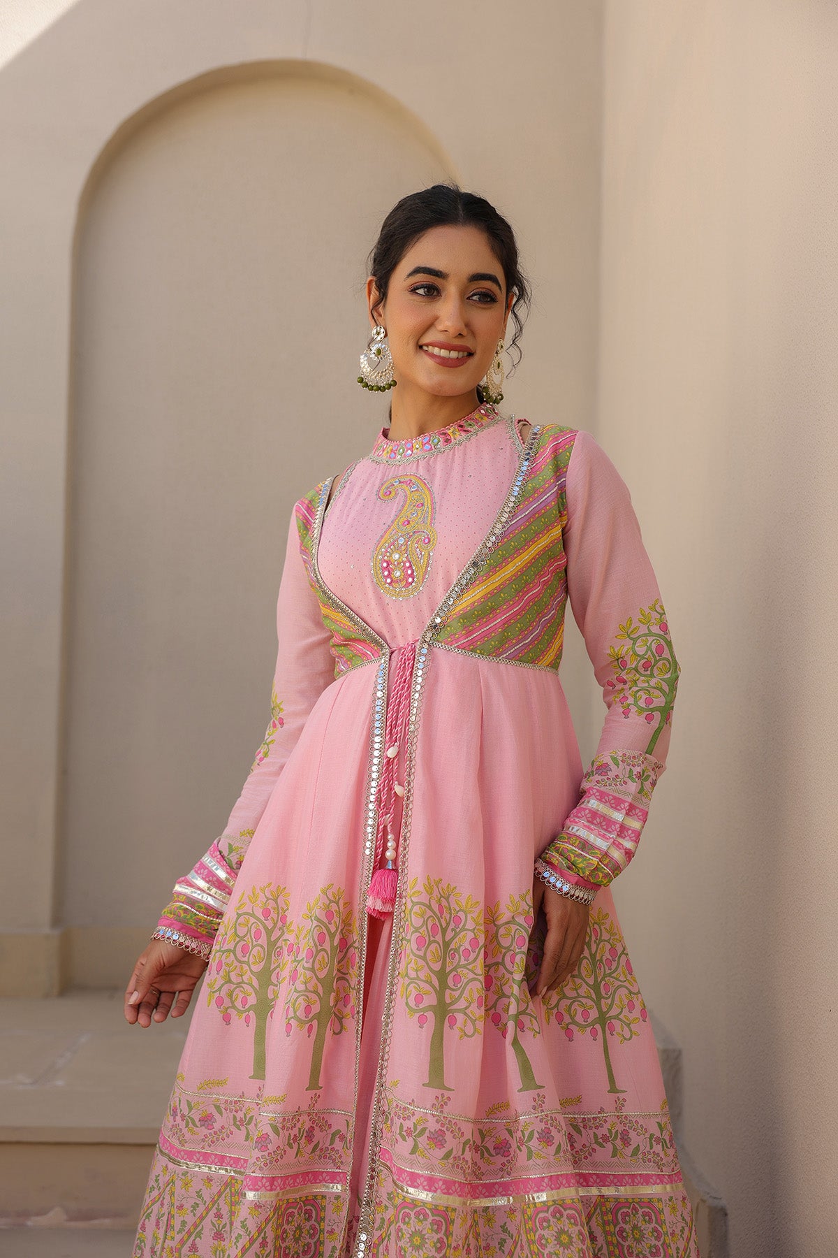 Woman wearing a traditional pink outfit with intricate patterns in an indoor setting.
