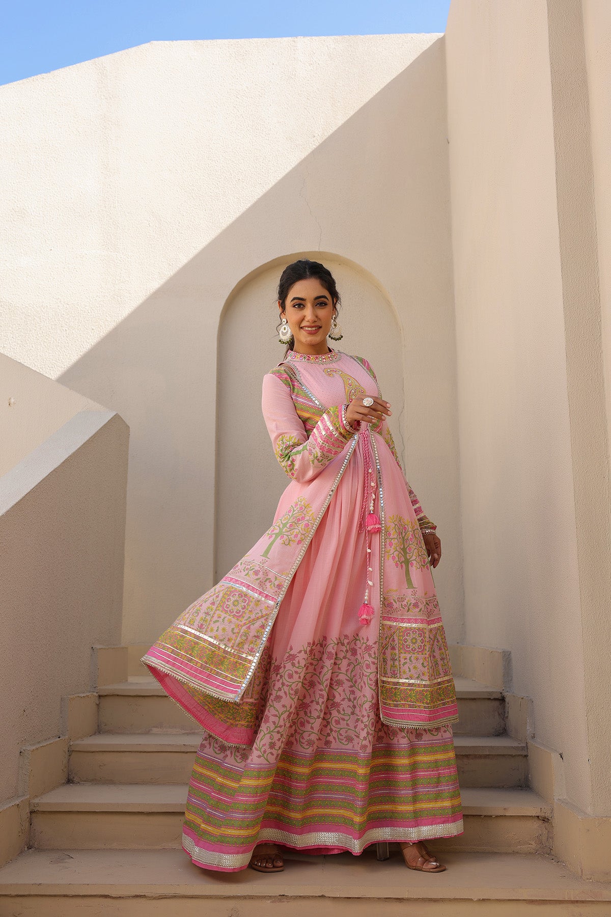 Woman in a traditional pink and gold outfit standing on steps with a white architectural background