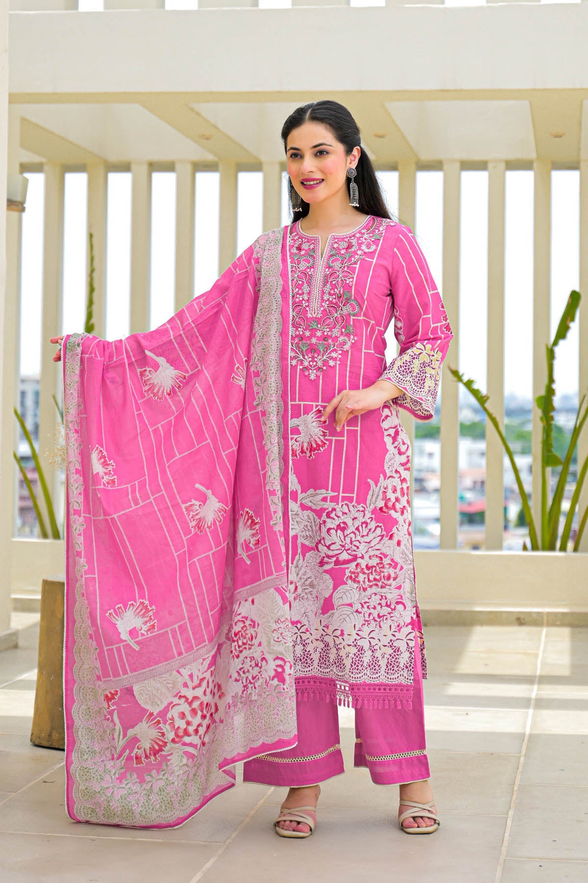 Woman wearing a pink embroidered outfit with a white border in an outdoor setting.
