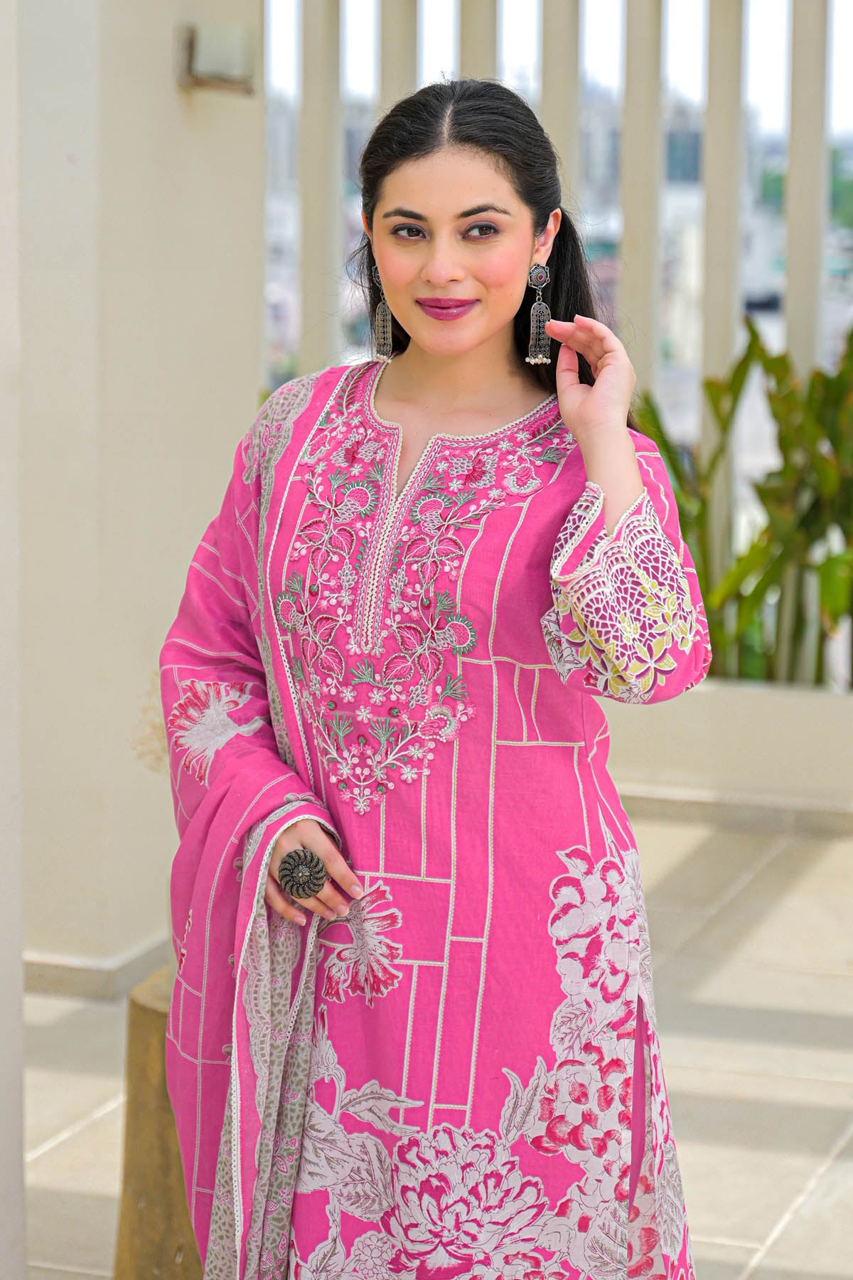Woman wearing a pink embroidered traditional outfit with a blurred outdoor background