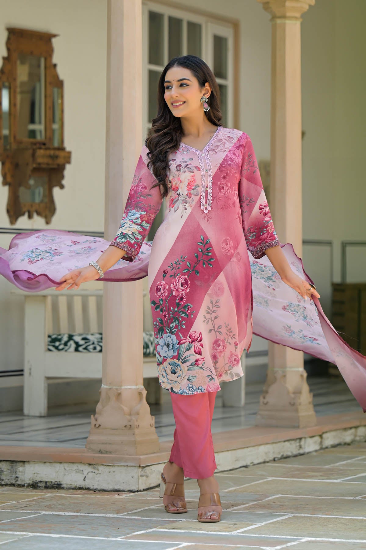 Woman in a pink embroidered outfit standing outdoors on a stone patio.