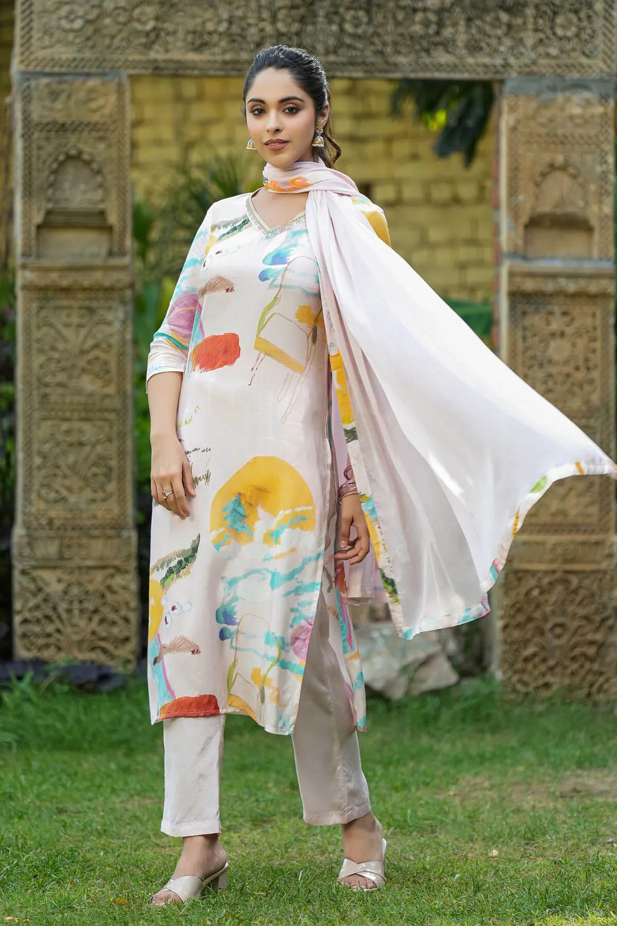 Woman in a floral dress standing outdoors with decorative stone wall in the background