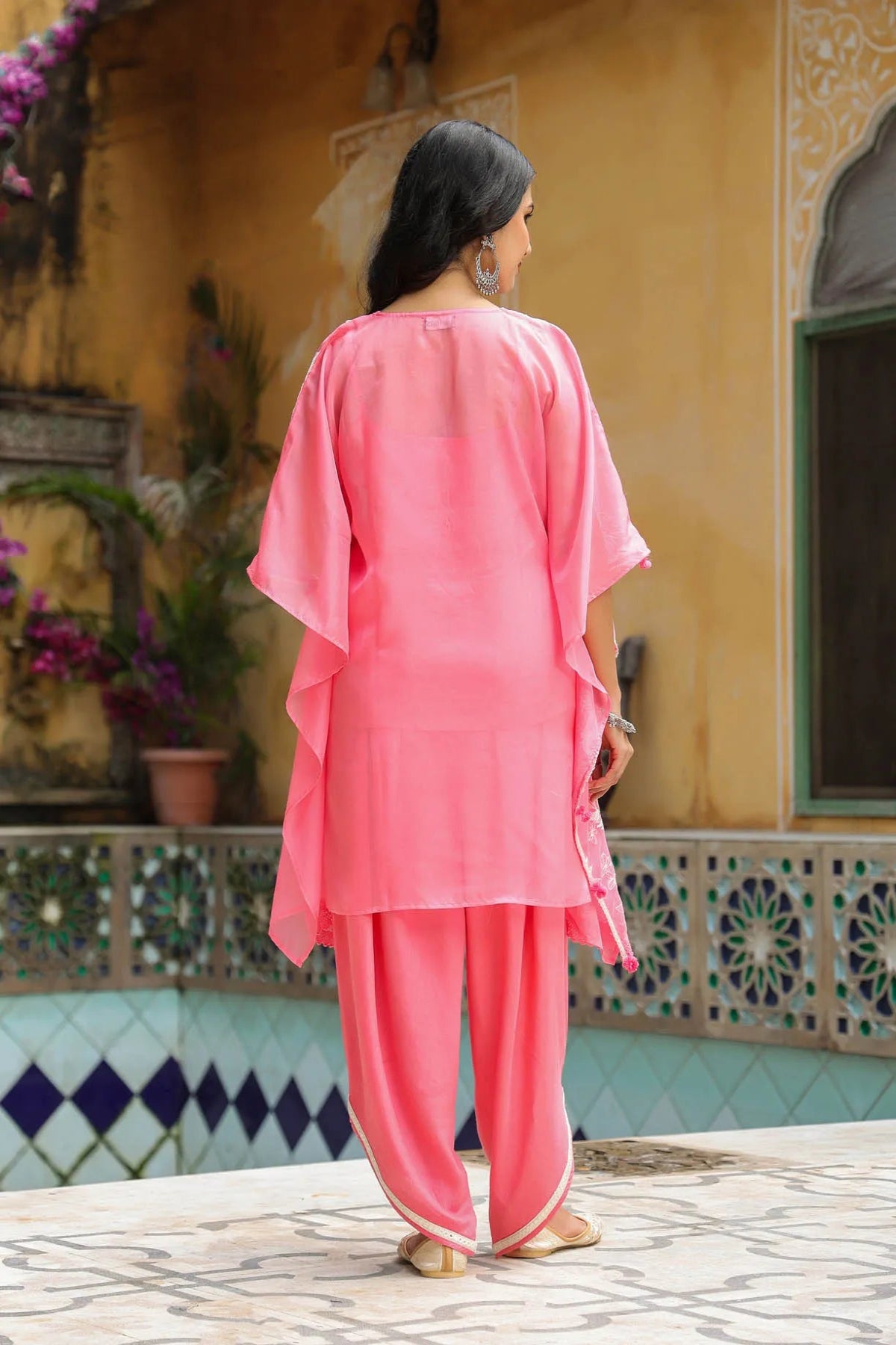 Woman in a pink traditional outfit standing in front of a decorative wall.