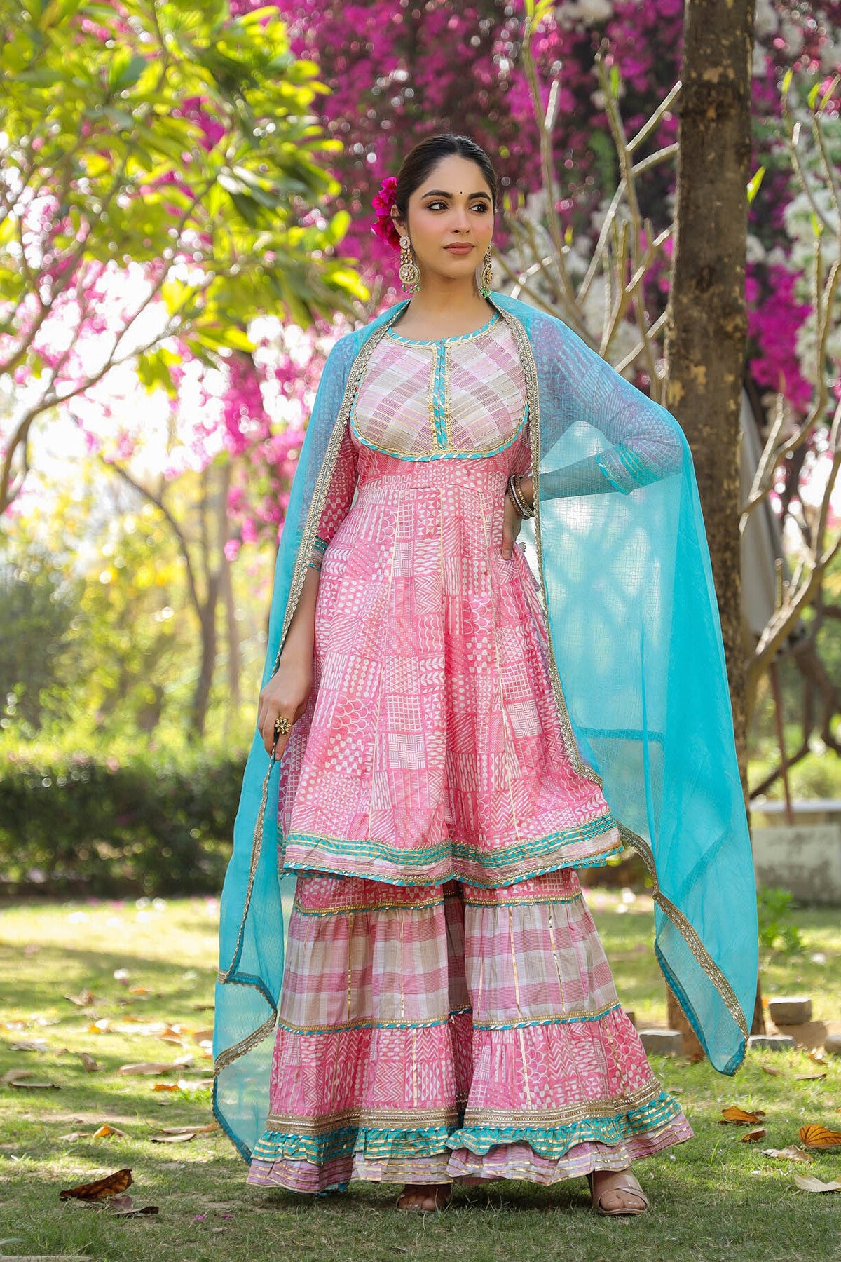 Woman in a pink traditional outfit with a blue dupatta standing in a garden.