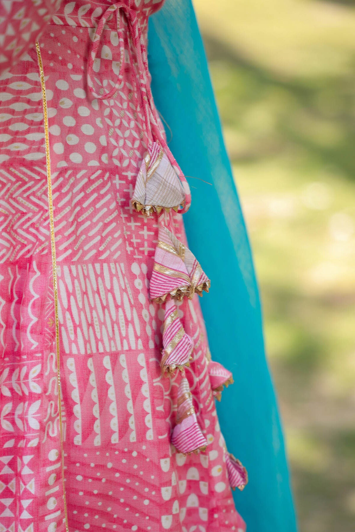 Close-up of a pink dress with white patterns and ruffled details, blurred green background