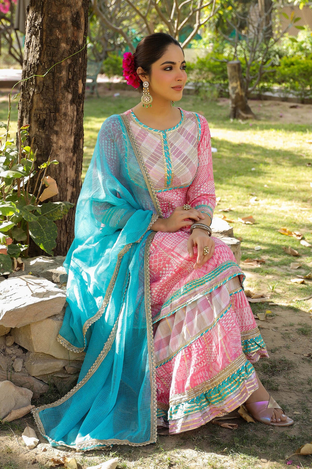 Woman in a pink and blue traditional outfit sitting outdoors.