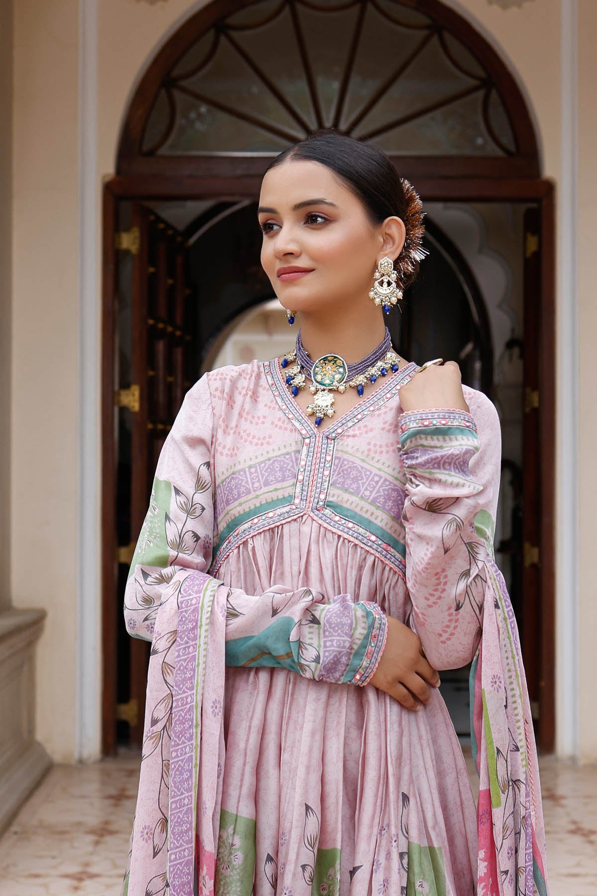 Woman in a traditional outfit with jewelry standing in front of an archway.
