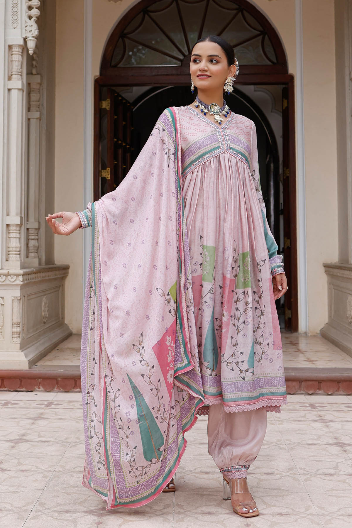 Woman in a traditional pink and green outfit standing in front of an archway.
