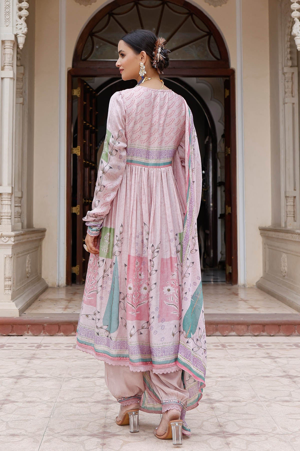Woman in a traditional outfit standing in front of an architectural entrance.