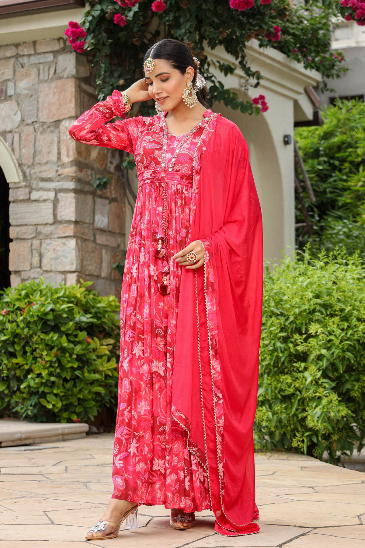 Woman in a red floral dress with a matching dupatta standing outdoors.