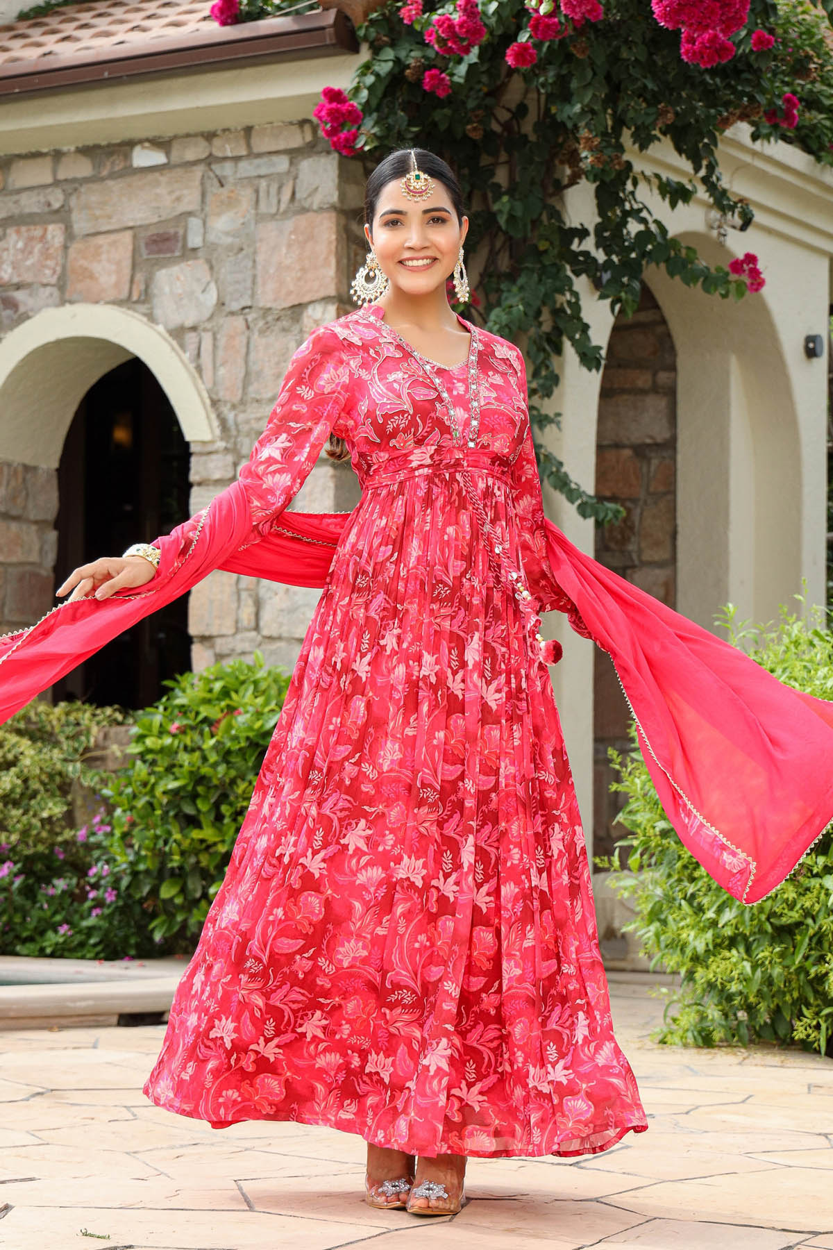 Woman in a red floral dress standing outdoors with decorative arch and flowers in the background