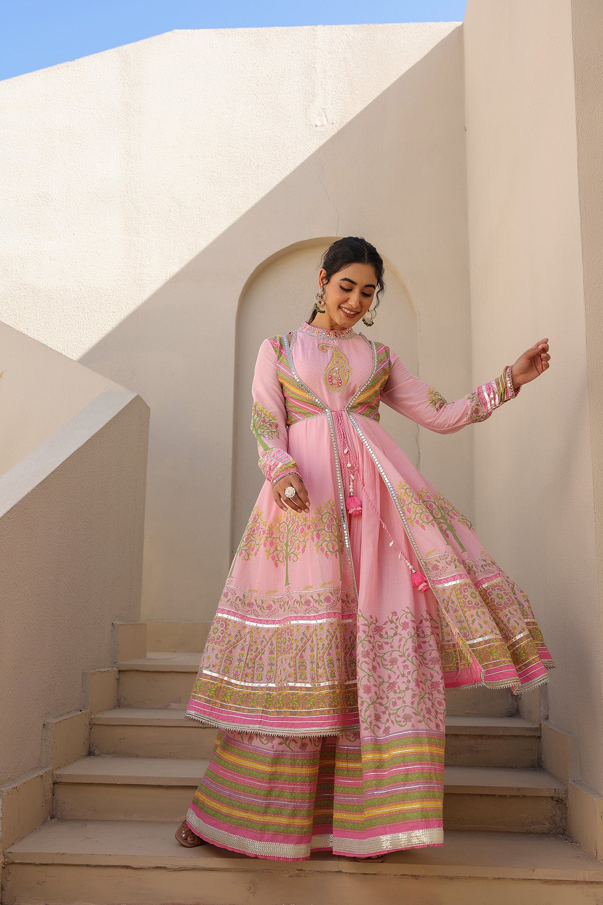 Woman in a pink traditional outfit standing on steps with a white architectural background