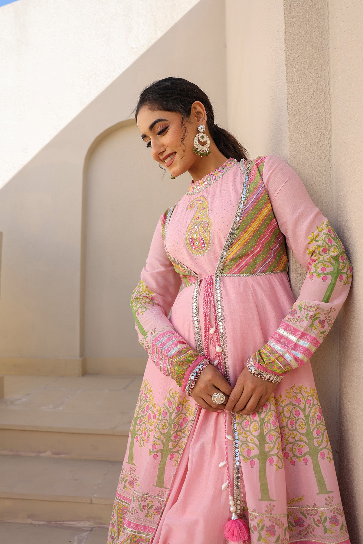 Woman wearing a pink traditional outfit with intricate patterns in an outdoor setting.