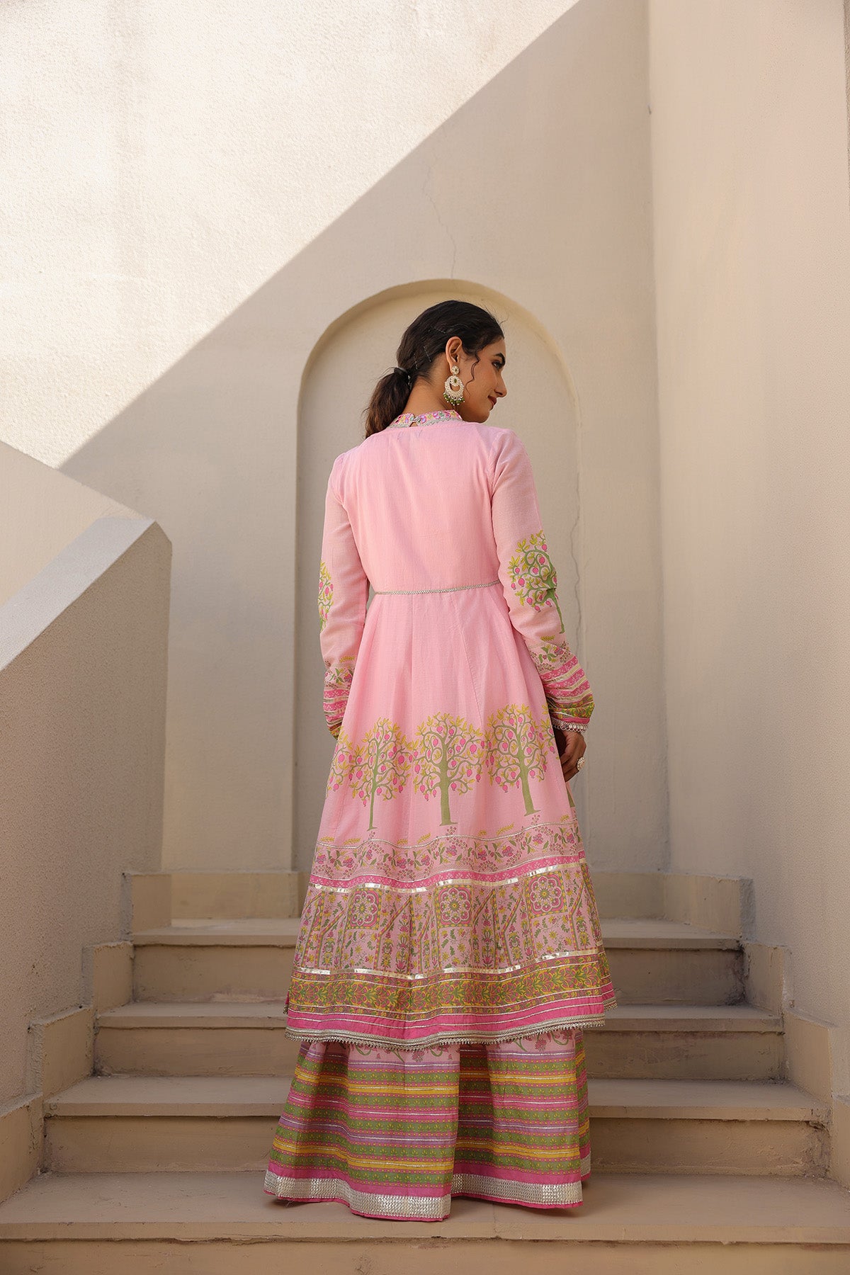 Woman in a pink traditional outfit standing on steps with a neutral background