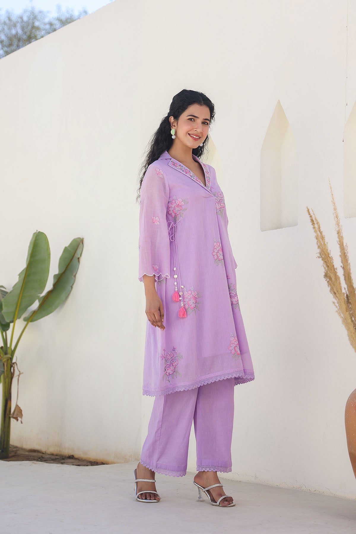Woman wearing a lavender outfit with floral embroidery against a white wall.