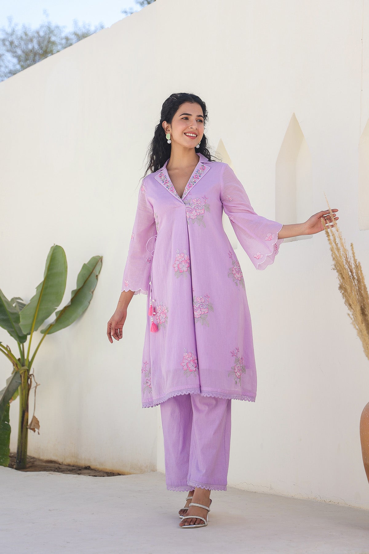 Woman wearing a light purple embroidered outfit with a white background