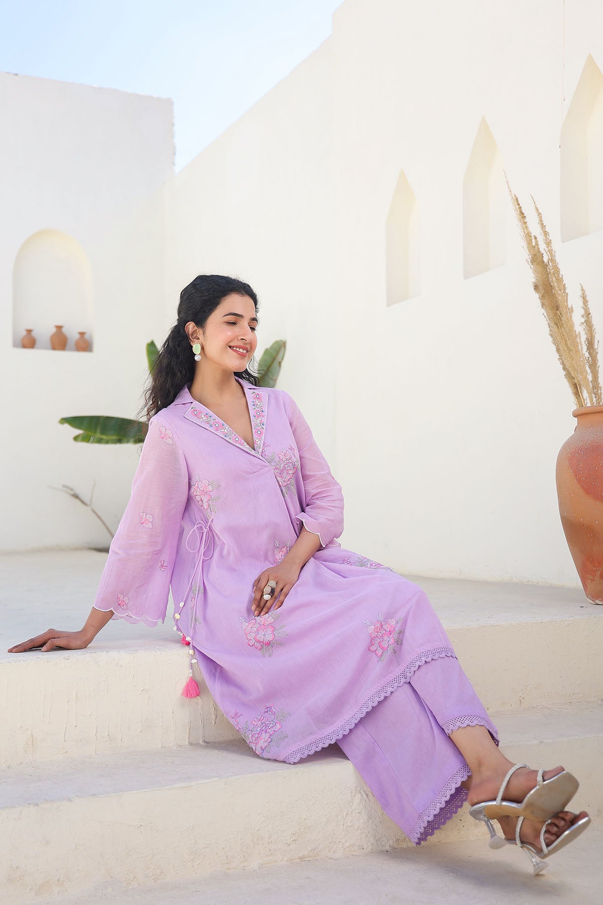 Woman in a lavender traditional outfit sitting on steps with a white background