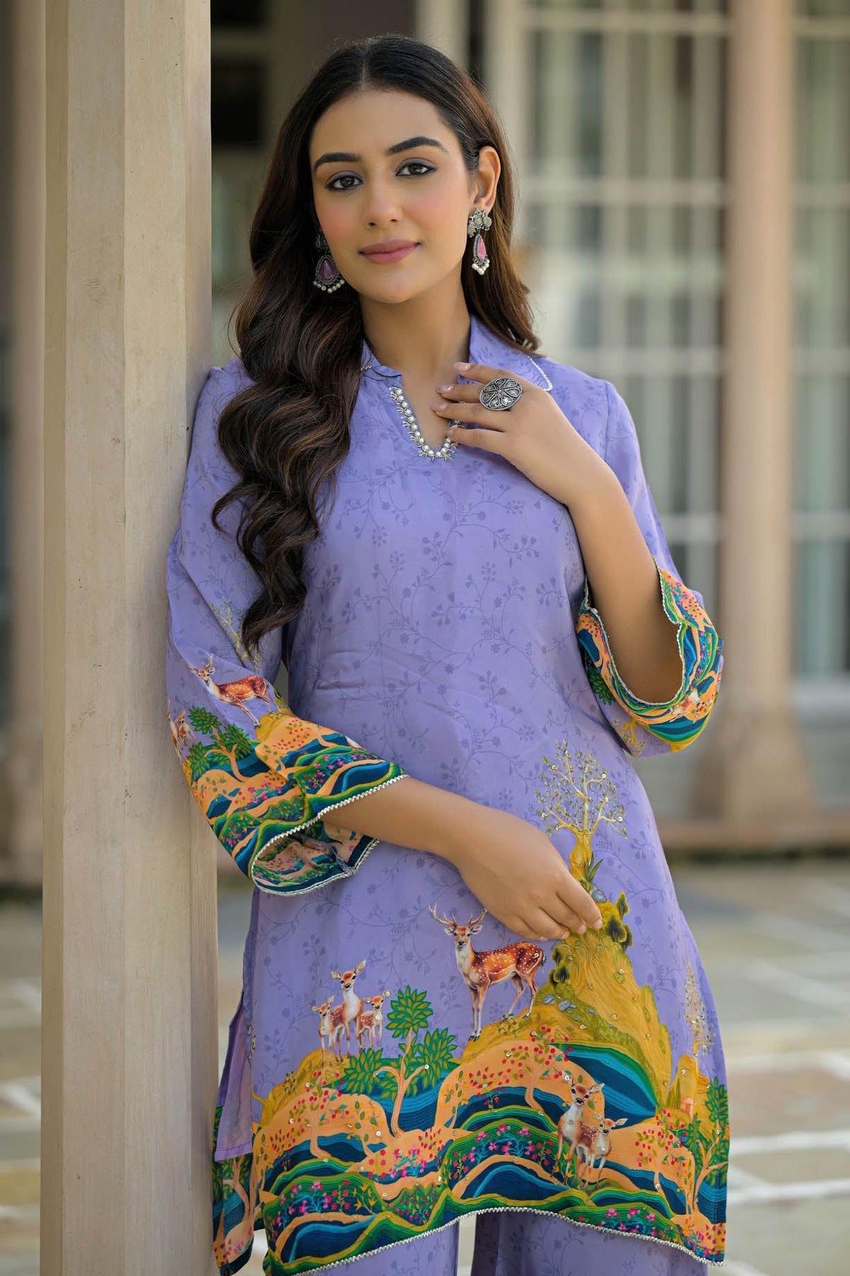 Woman wearing a purple embroidered outfit with a scenic design, standing indoors.