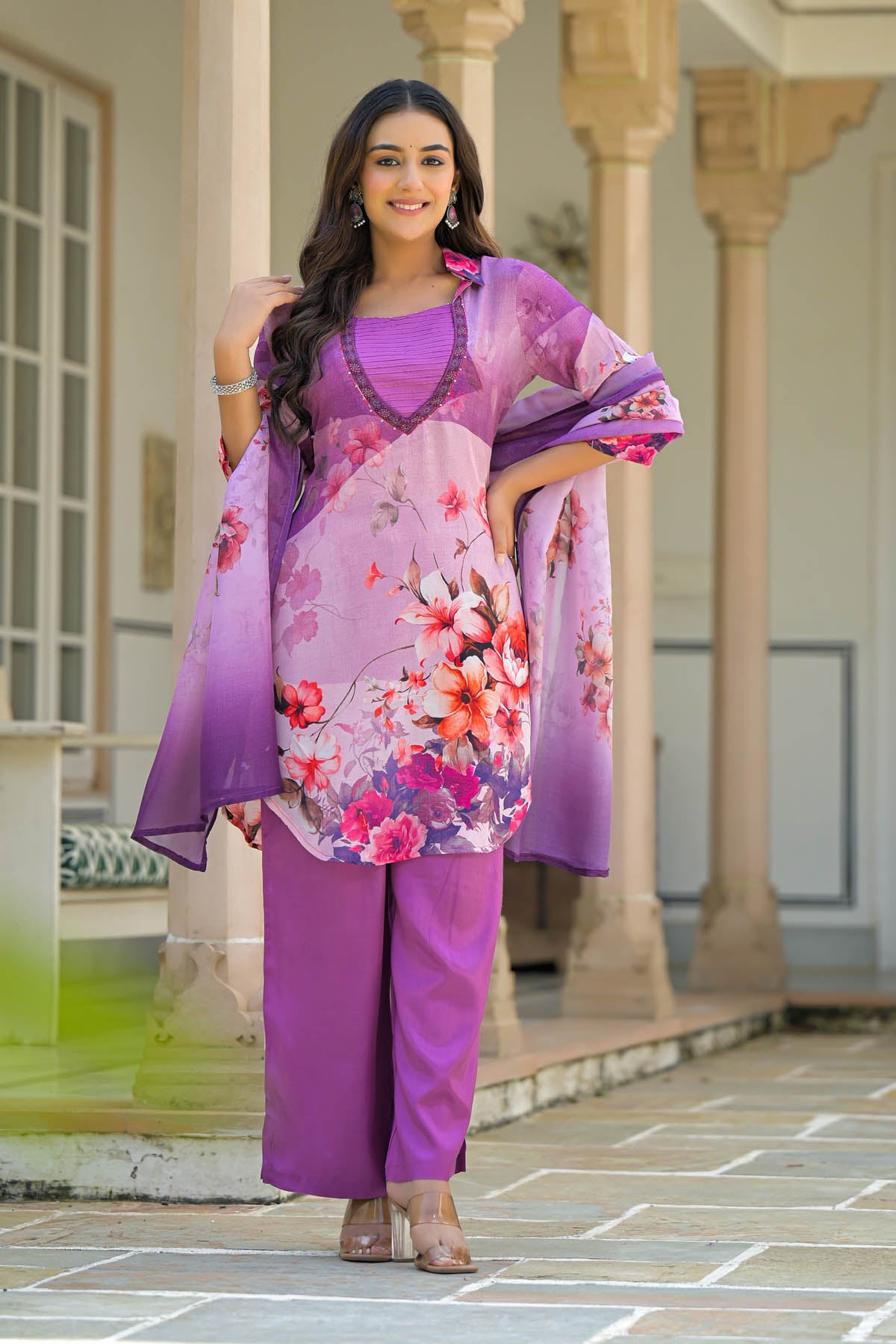Woman in a purple floral outfit standing in front of architectural columns.