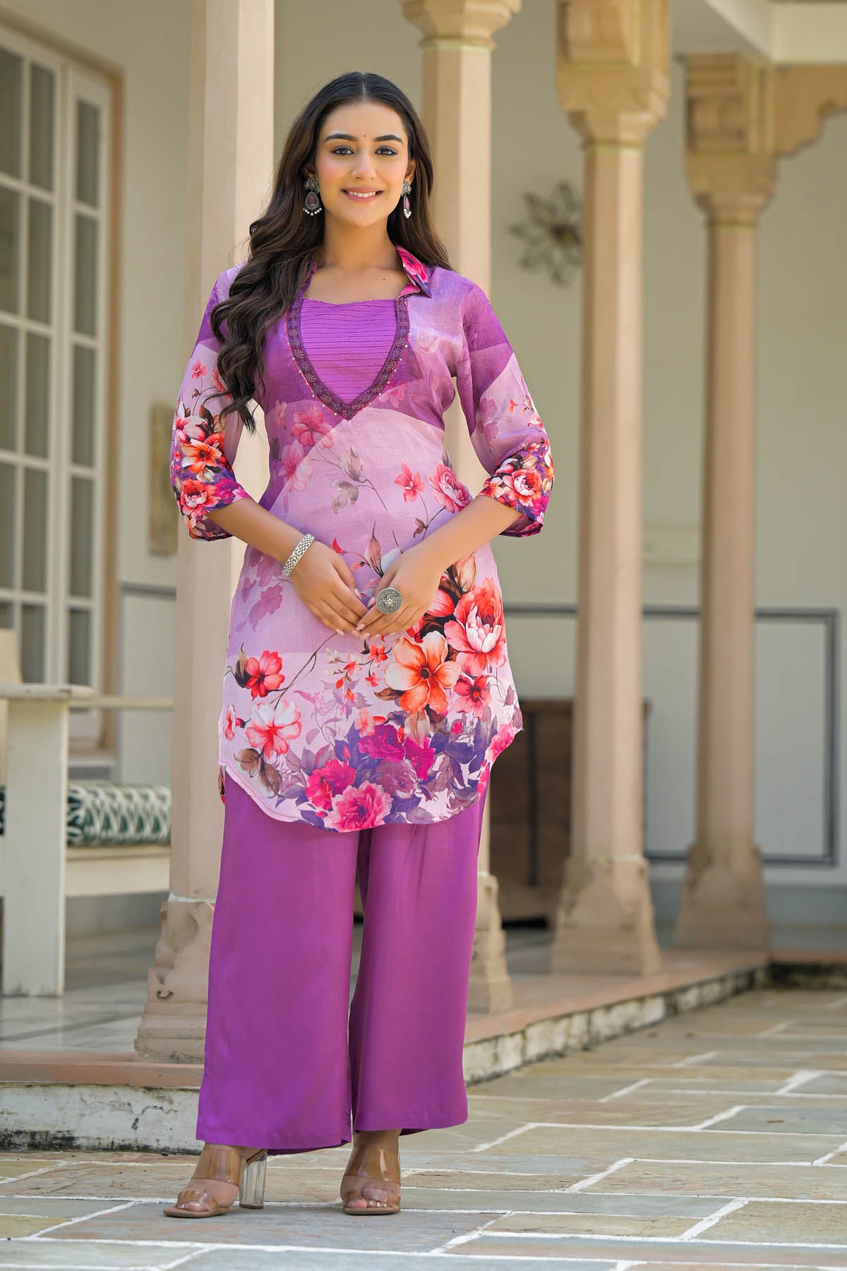 Woman wearing a floral dress with a purple top and pants in an outdoor setting.
