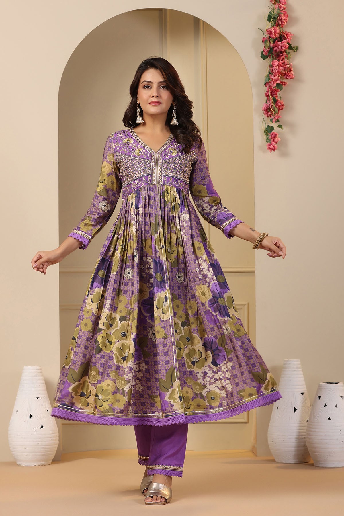 Woman wearing a purple floral dress standing in a decorated room with vases and flowers.