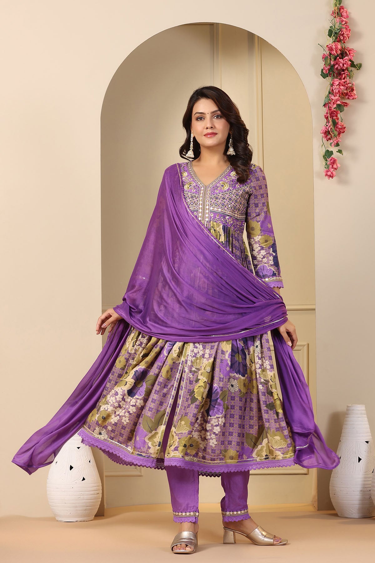 Woman wearing a purple traditional outfit with a floral design in a decorated room.