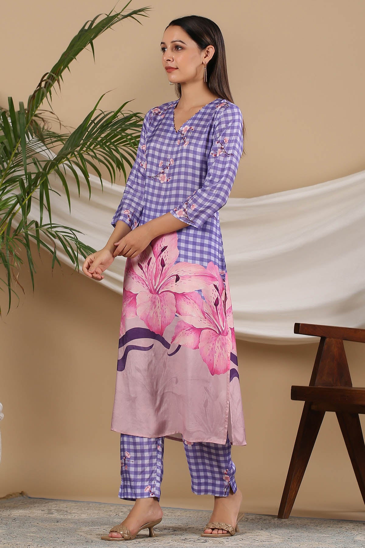 Woman wearing a purple and pink checkered kurta with floral pants against a beige wall.