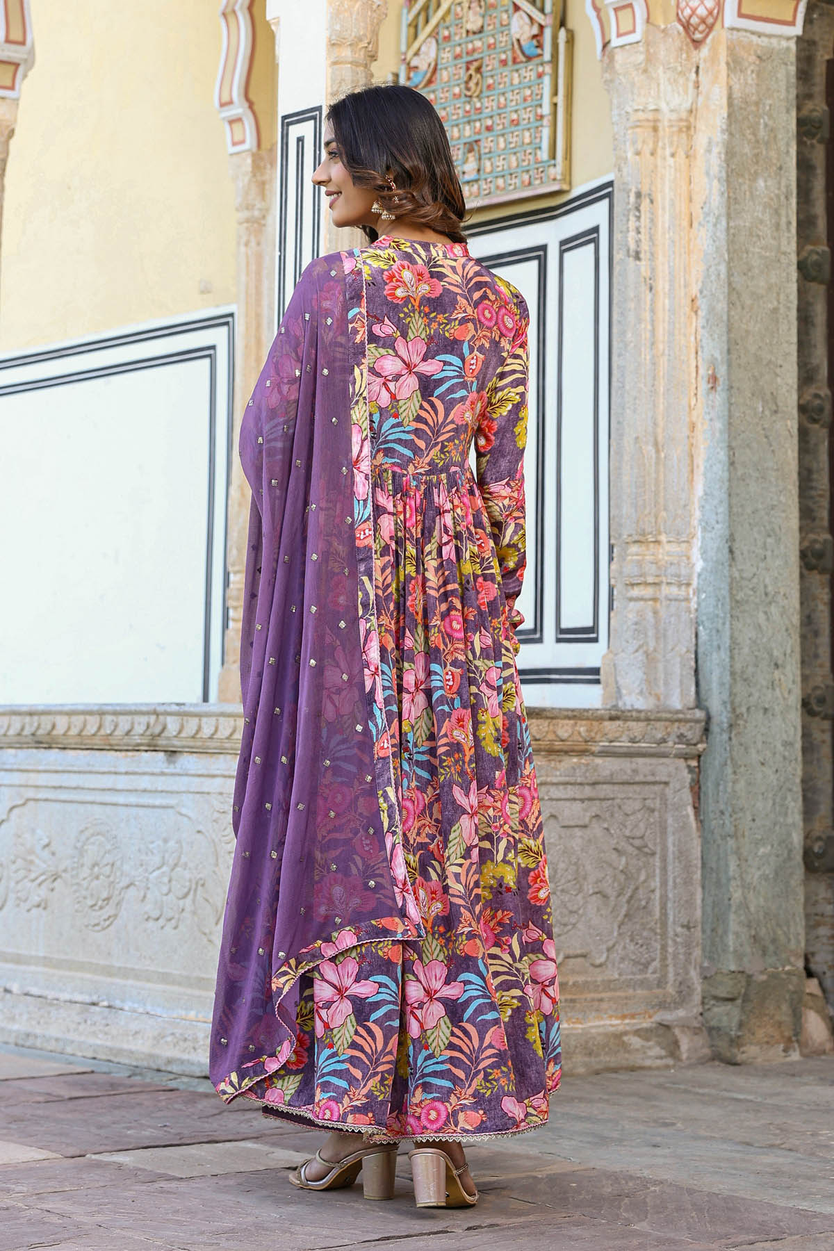Woman wearing a colorful floral dress with a purple shawl in an ornate architectural setting.
