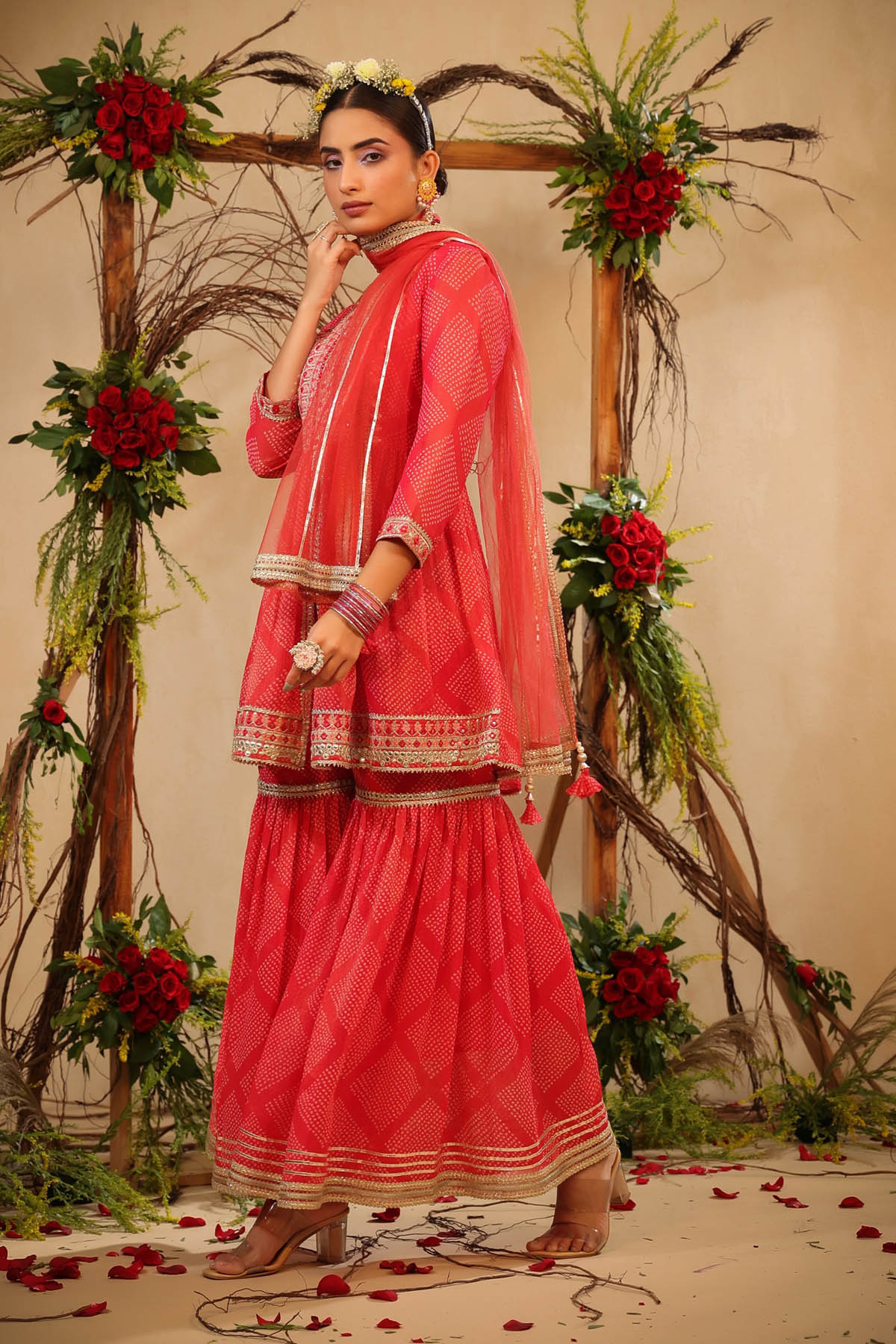 Woman in a traditional pink outfit standing in front of floral decorations.