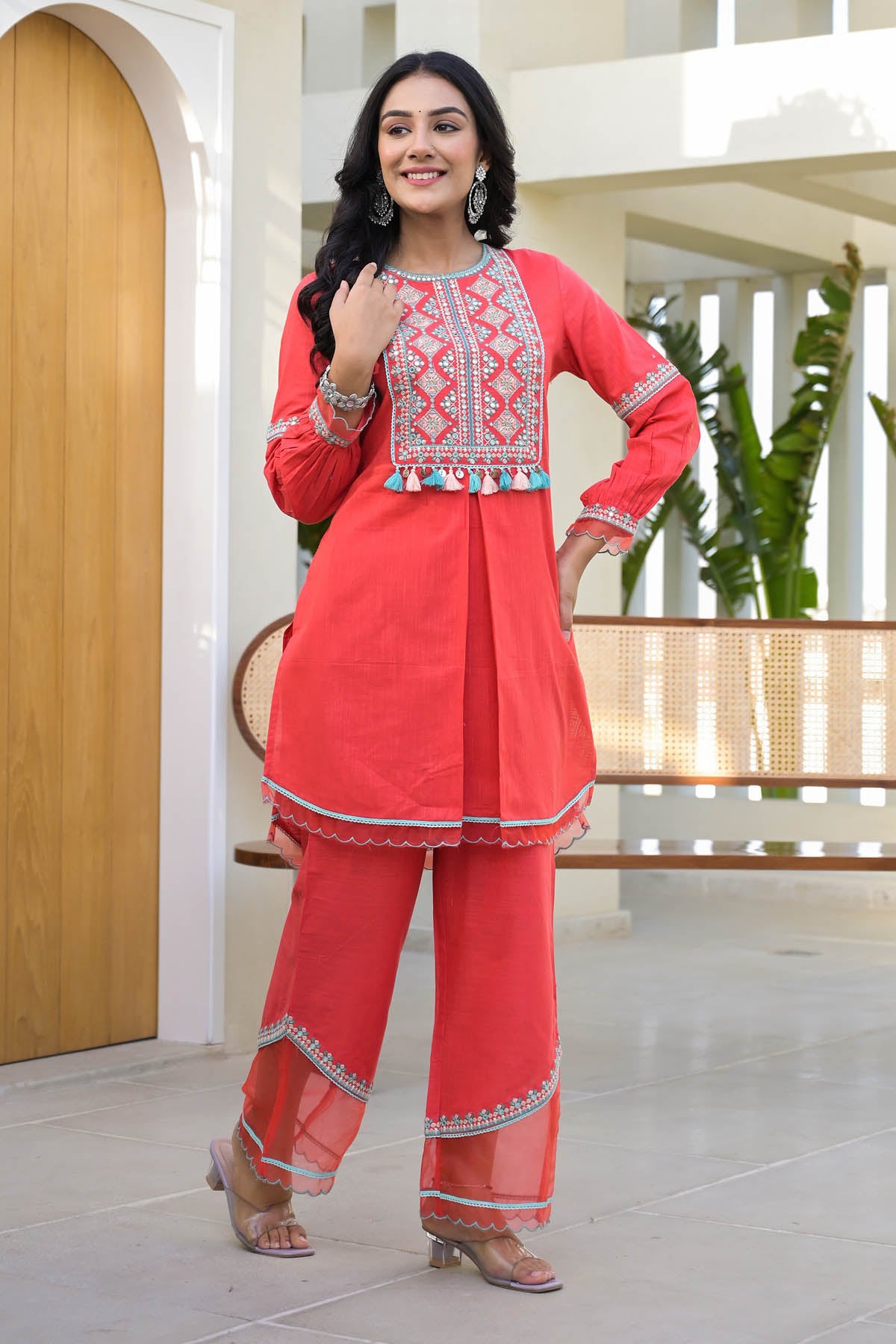 Woman wearing a red traditional outfit with white patterns in an indoor setting.