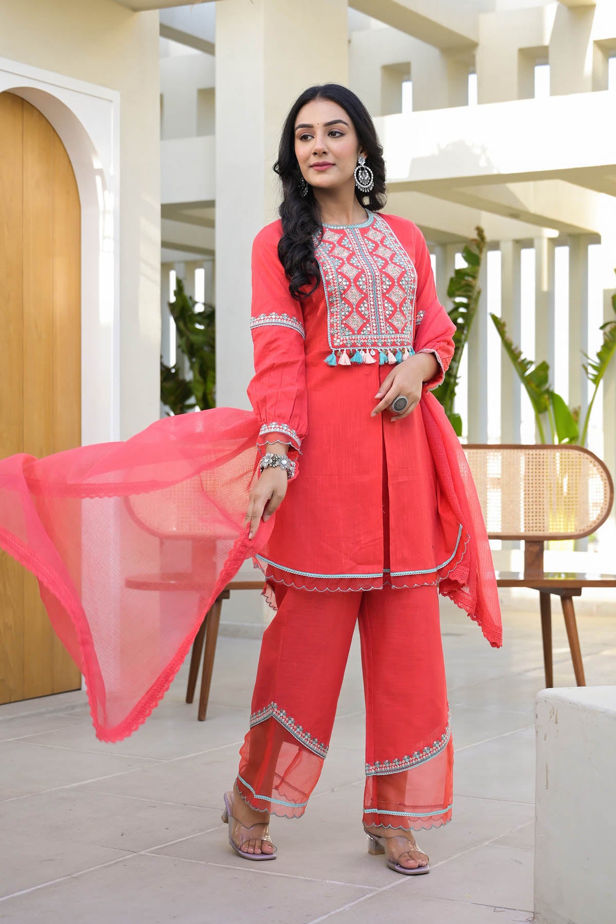 Woman in a coral traditional outfit with intricate patterns indoors.