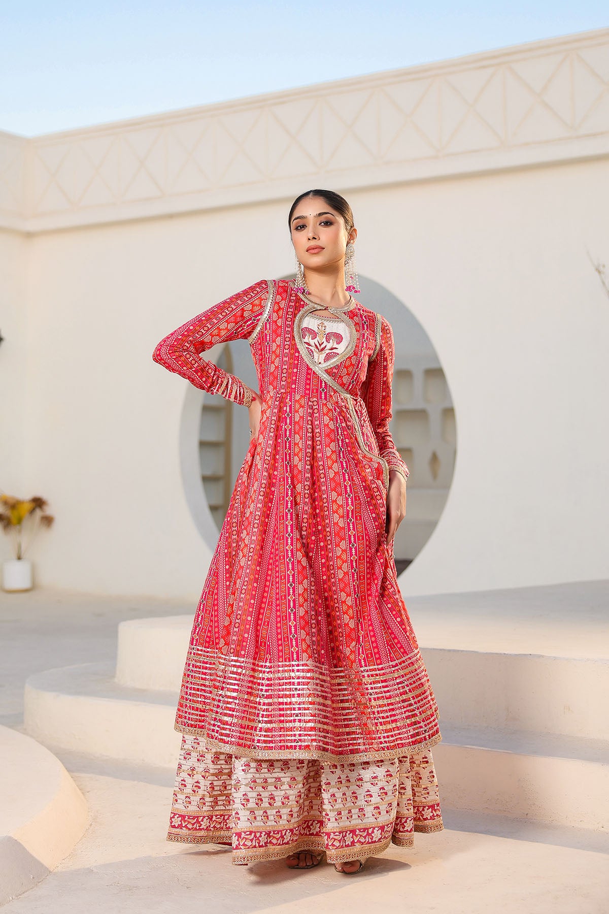 Woman in a red and white traditional outfit standing in front of a decorative archway.