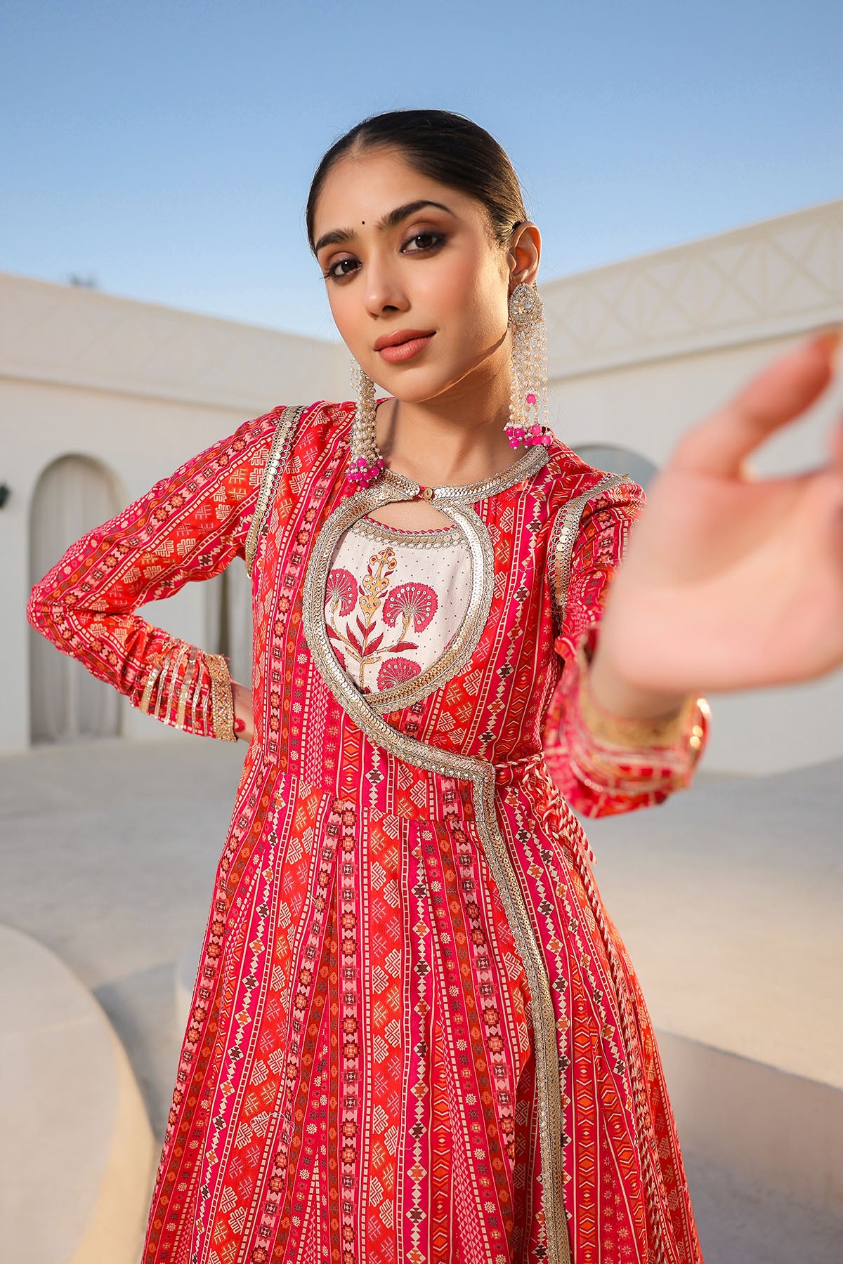 Woman in a red traditional outfit with intricate patterns and jewelry, standing outdoors.