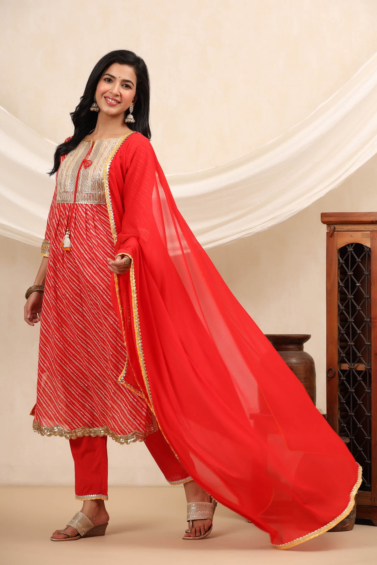 Woman wearing a red traditional outfit with gold details against a beige background