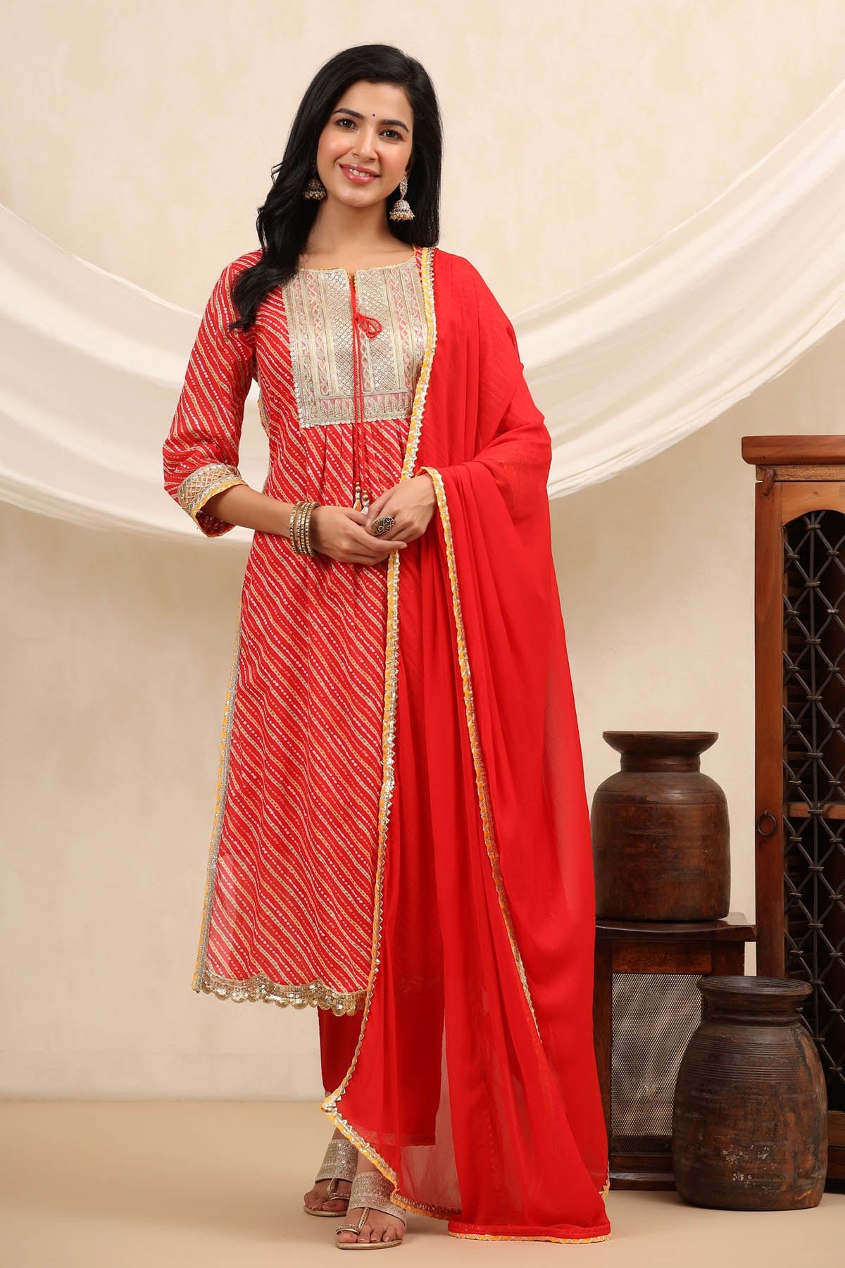 Woman wearing a red and white traditional outfit with a dupatta, standing against a neutral background.