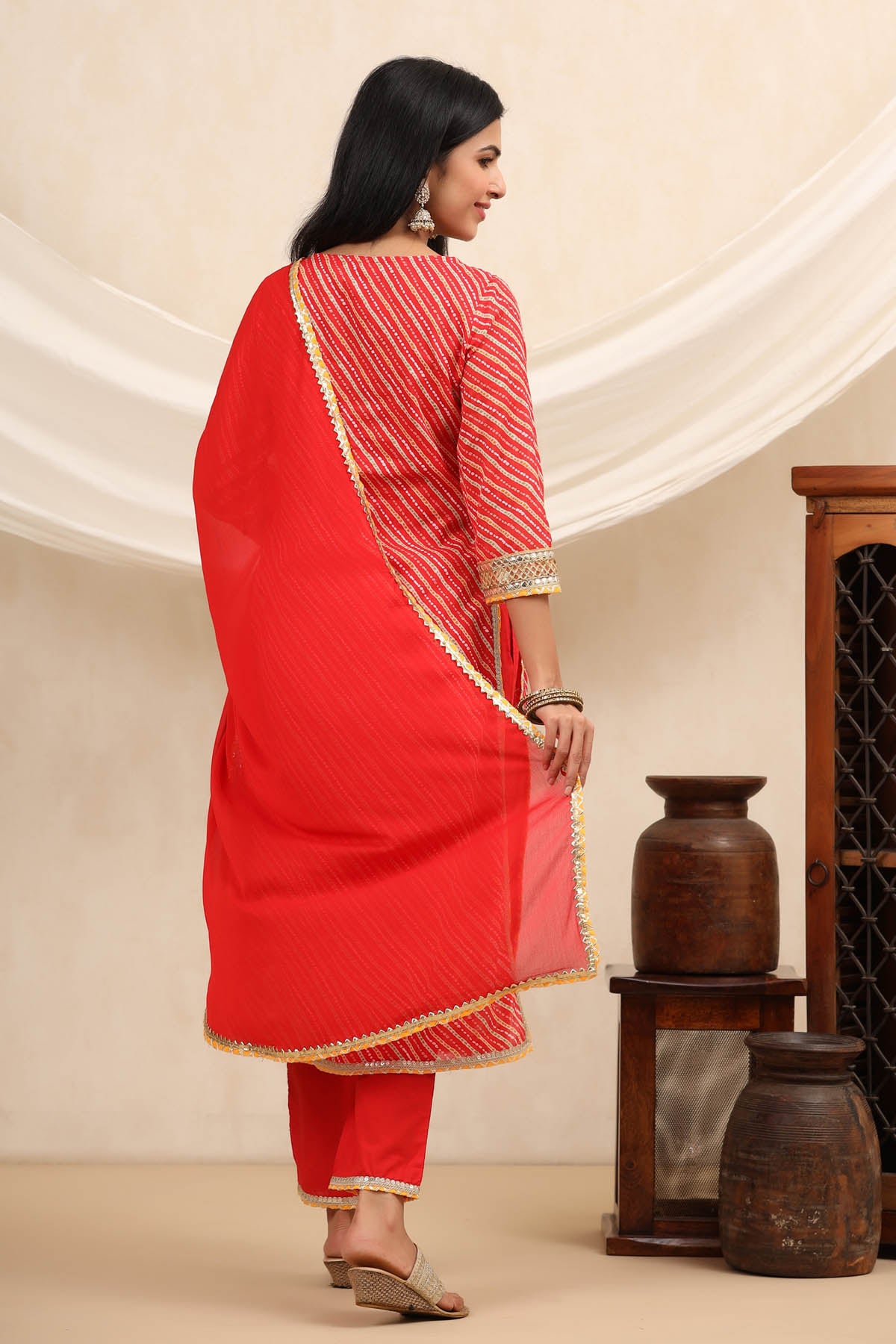 Woman wearing a red traditional outfit with gold accents in a minimalistic setting.