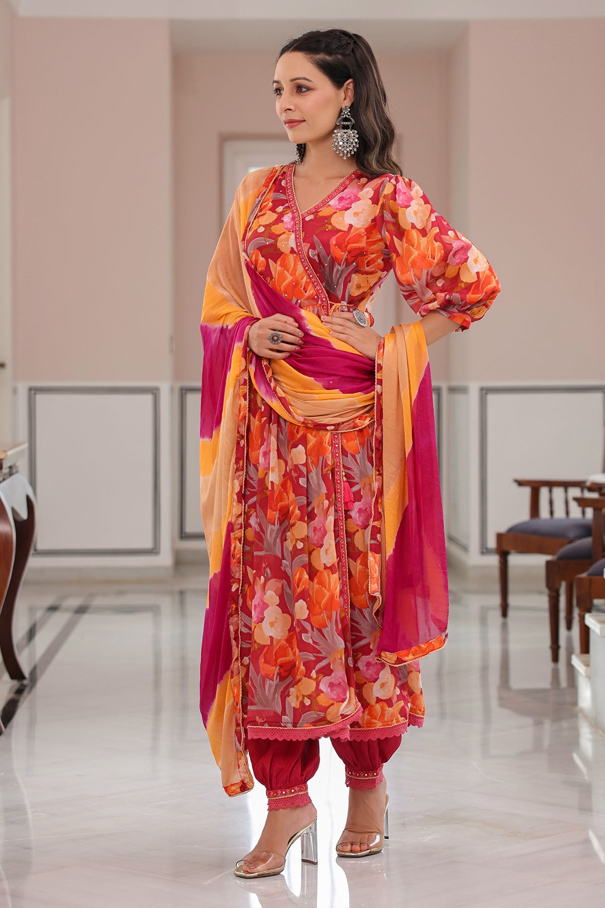 Woman in a colorful traditional outfit standing in a room with furniture.