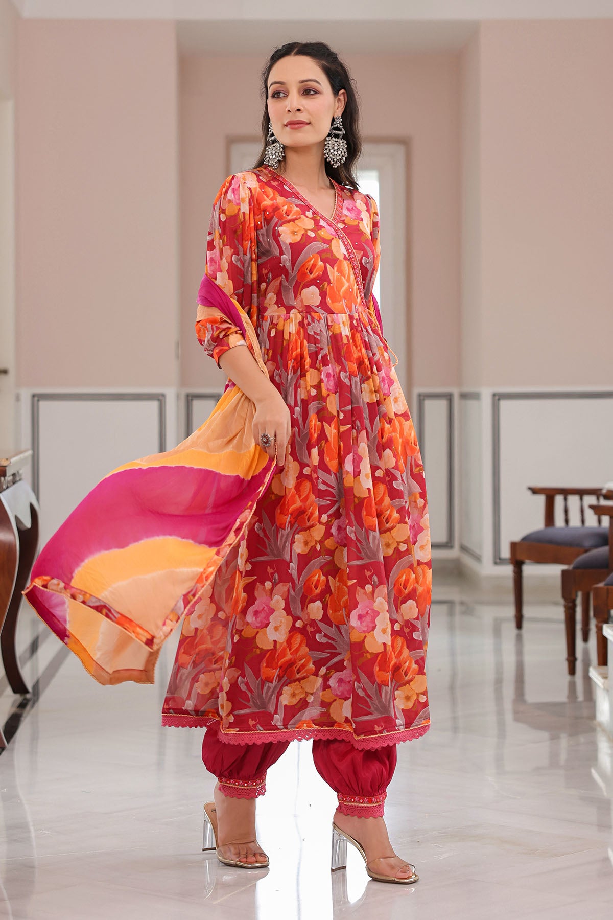 Woman in a vibrant floral dress holding a colorful bag in an indoor setting.