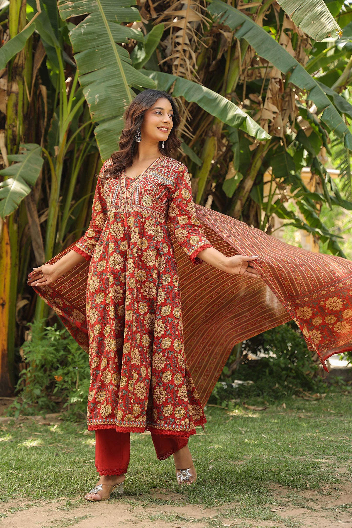 Woman in a red and gold traditional outfit with a flowing fabric in a natural setting