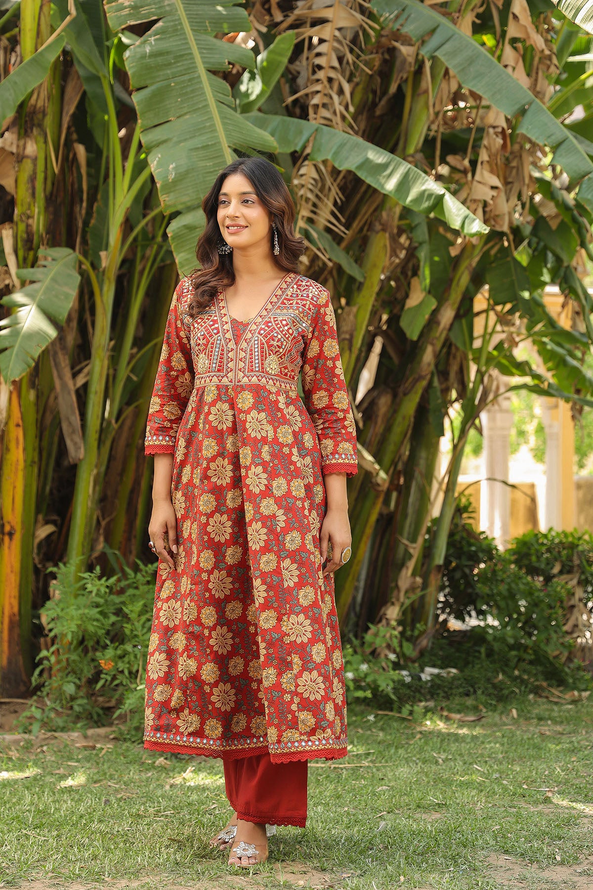 Woman in a red floral dress standing in a garden with green plants