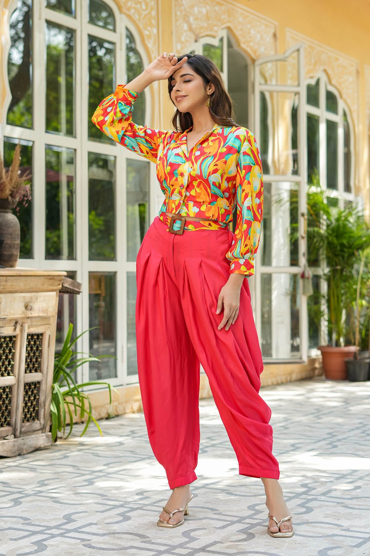 Woman in colorful top and red pants standing in a decorative outdoor setting.