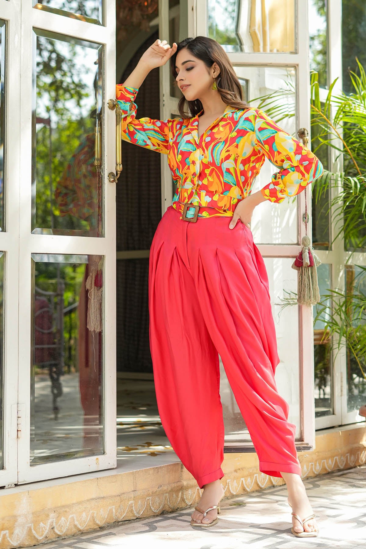 Woman in colorful top and red pants posing in front of a glass door.