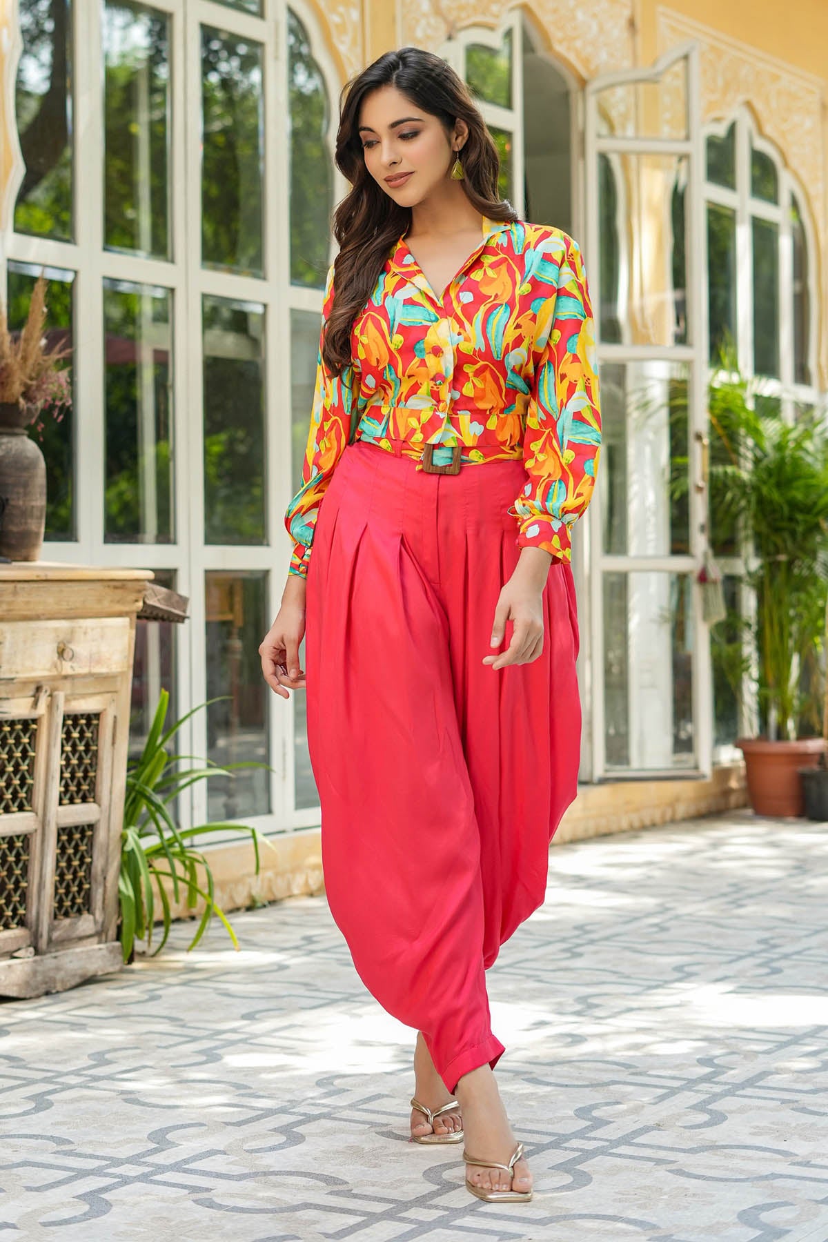 Woman in colorful blouse and red pants standing outdoors with a building in the background