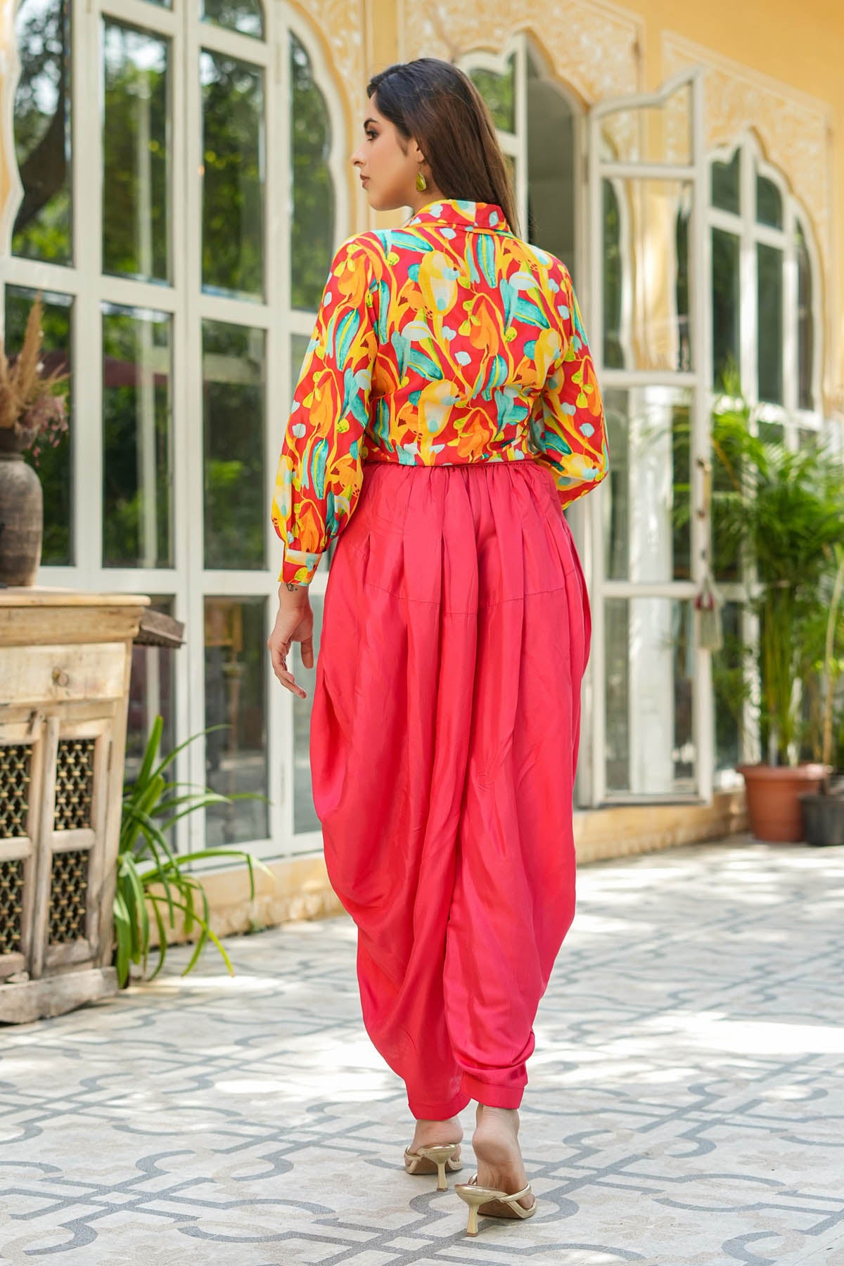 Woman in colorful top and pink dhoti pants walking outdoors.