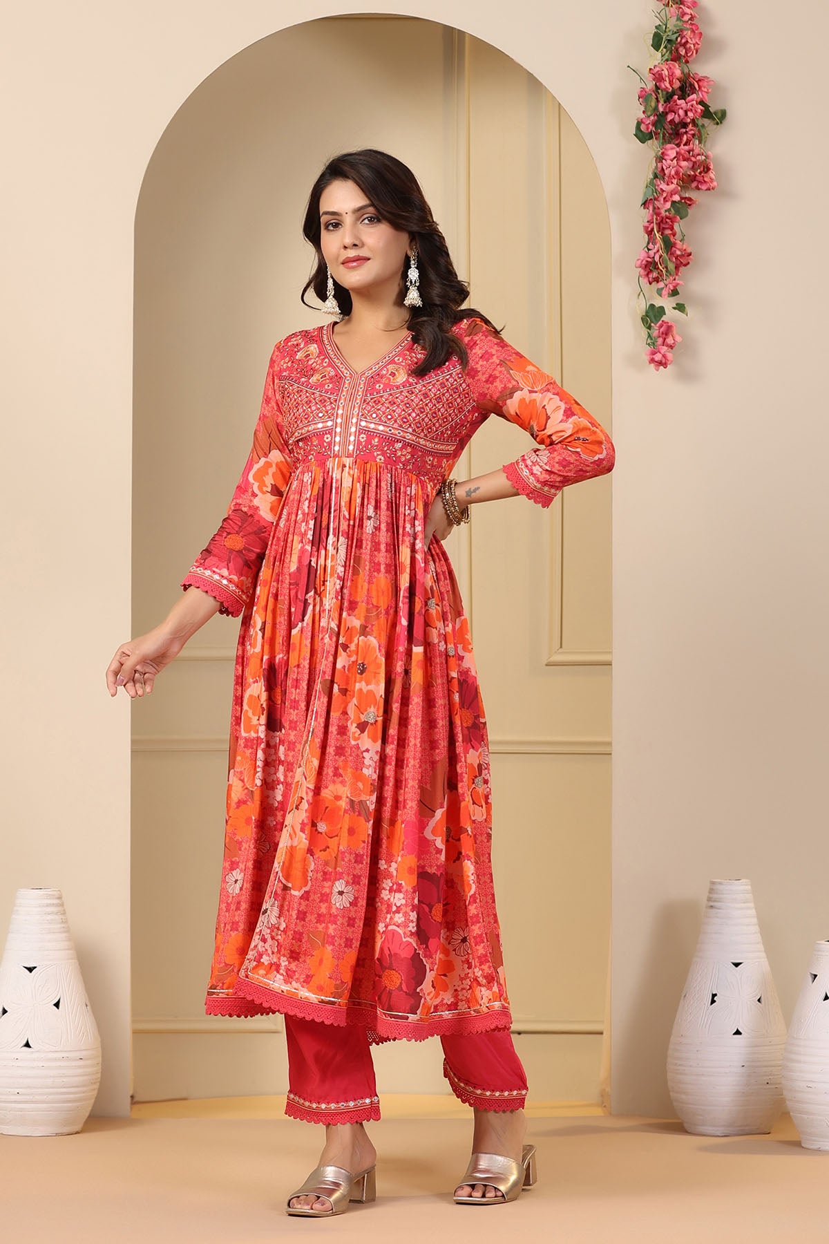 Woman wearing a vibrant orange and pink traditional outfit standing in a decorated room.
